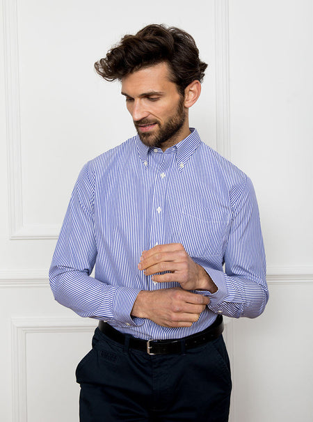 Man wearing long sleeved shirt with royal blue and white thin stripe made with 100% cotton from Thomas Mason.